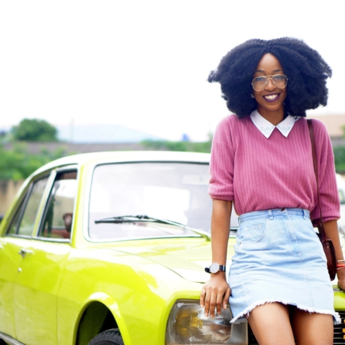 nigerian lifestyle blogger Cassie daves wearing a denim mini skirt. leaning against a lemon green peugeot 504