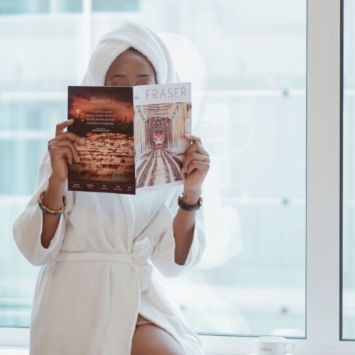 Cassie daves in a robe holding a magazine at fraser suites abuja